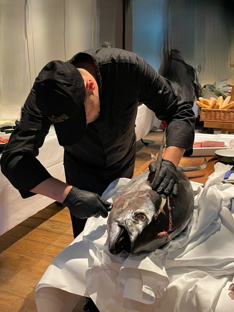 Koch bereitet frischen Fisch auf einem Tisch in einem eleganten Ambiente zu.